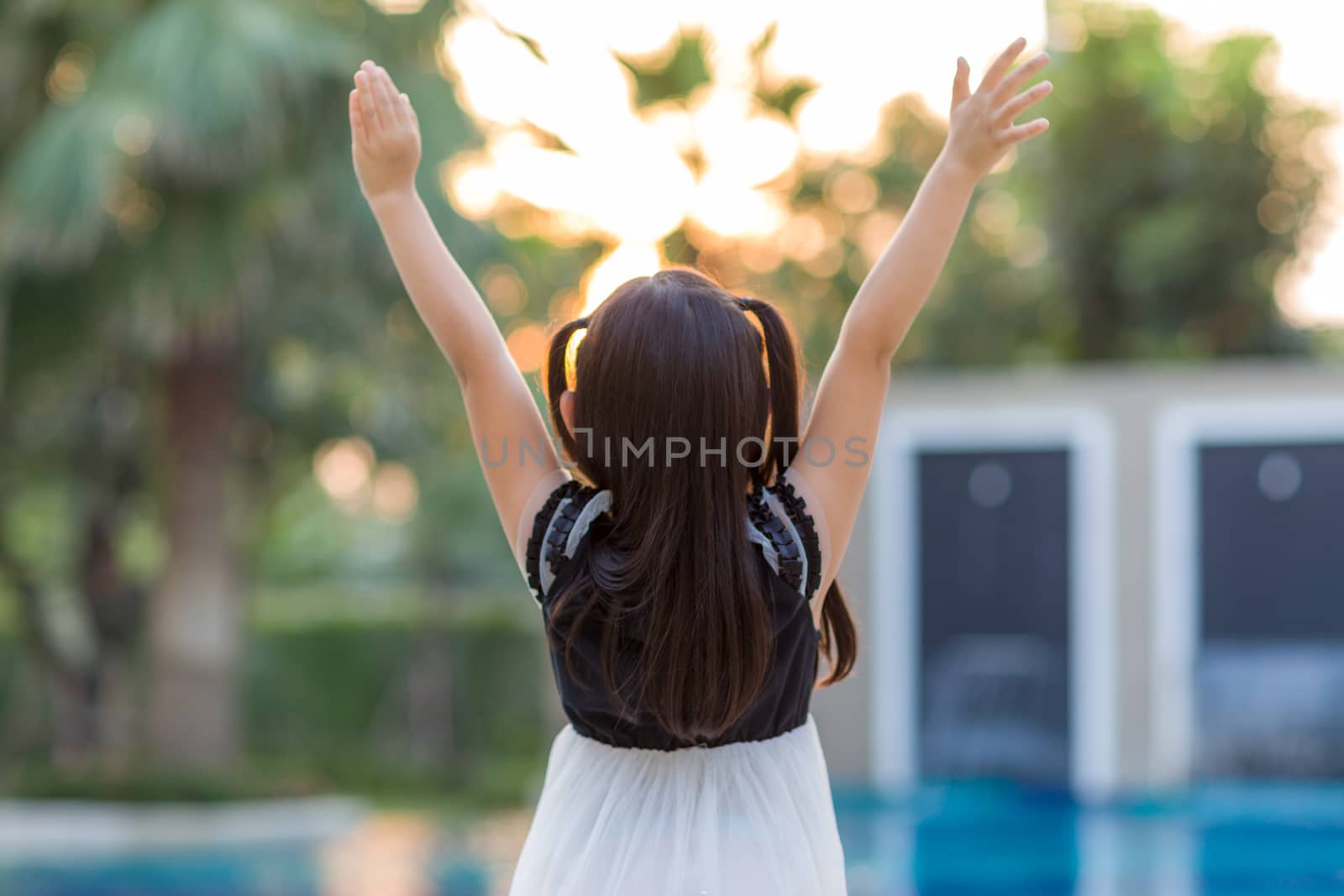 Child raising hands and facing the sun.