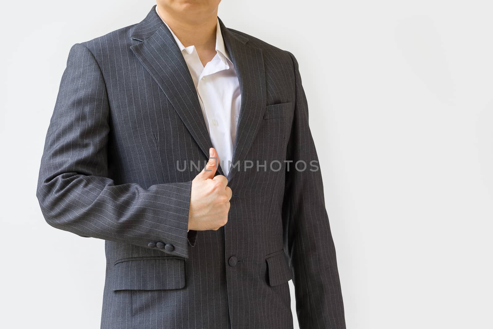 Concept of success illustrated by studio shot of businessman in suit showing thumb up, isolated on white.