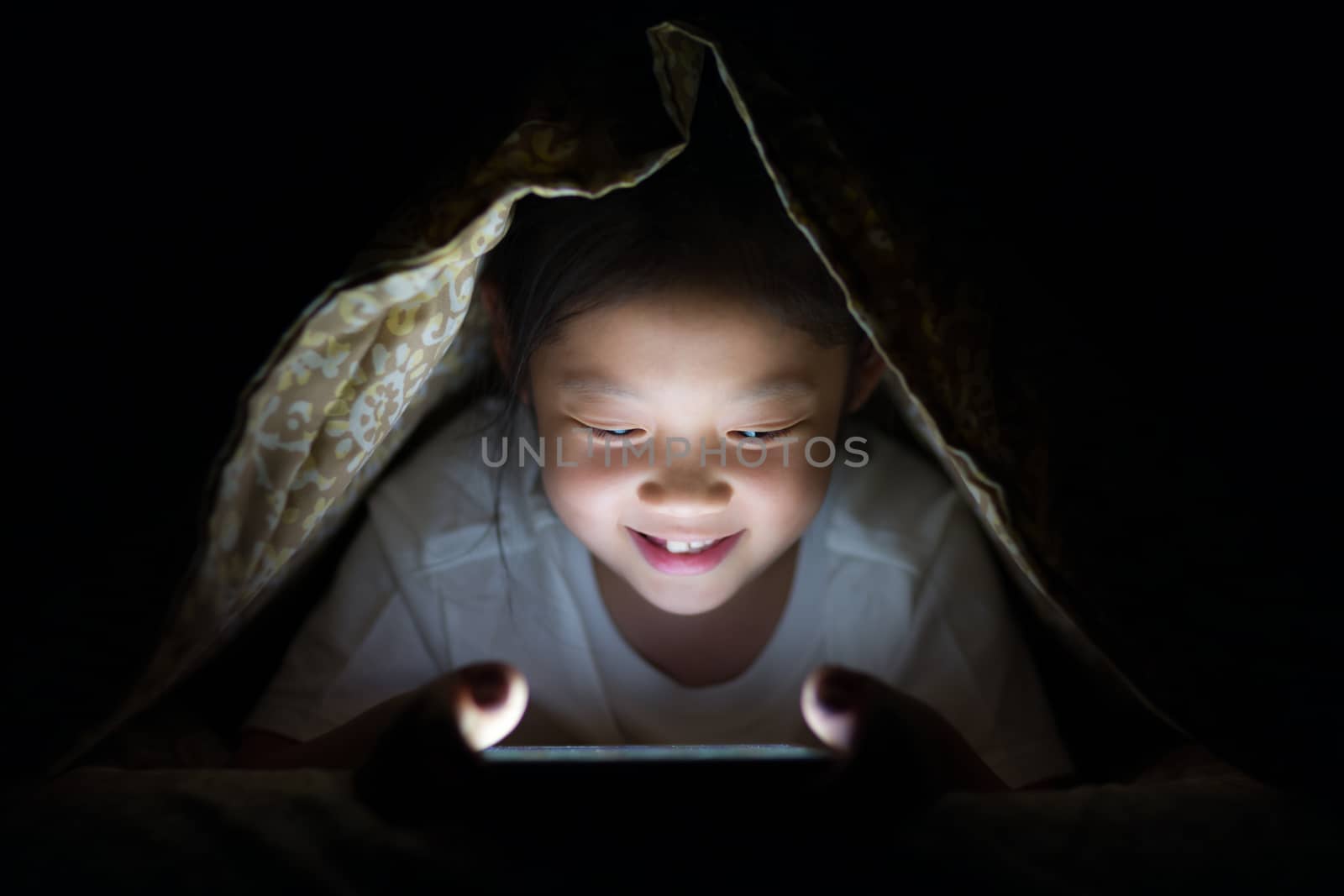 Happy Asian child using on tablet PC in her bed at night.