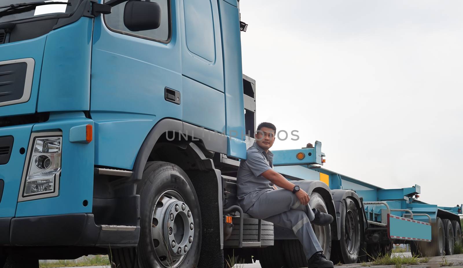 Asian young man Is a truck driver in the transportation business Equipped with large blue trucks Parking a car on the side of the road