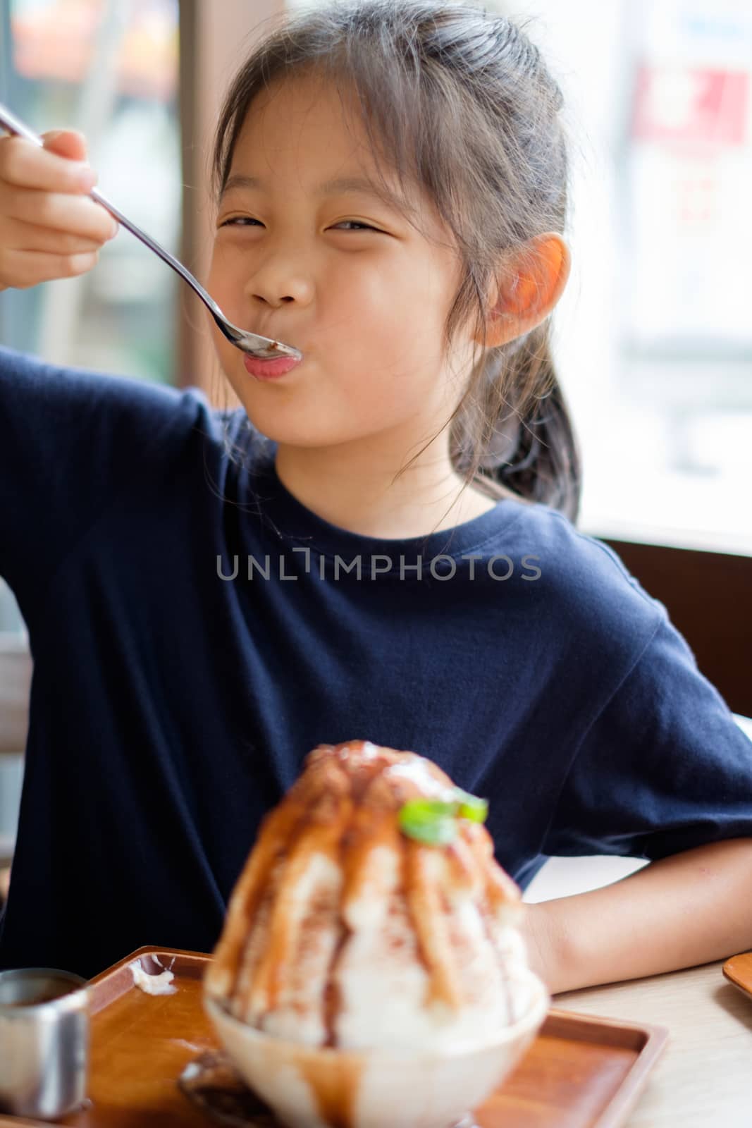 Happy Asian child enjoys eating shave ice frozen dessert.