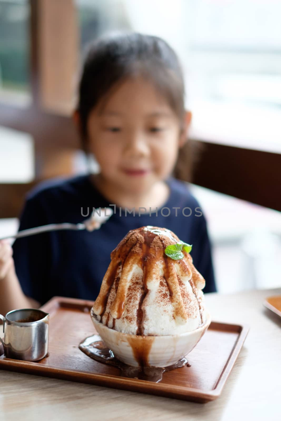 Happy Asian child enjoys eating Korean Patbingsu or Bingsu, shave ice frozen dessert.