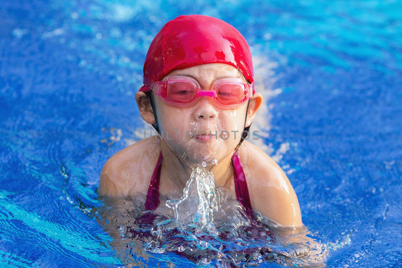 Child swimming breaststroke in outdoor swimming pool.