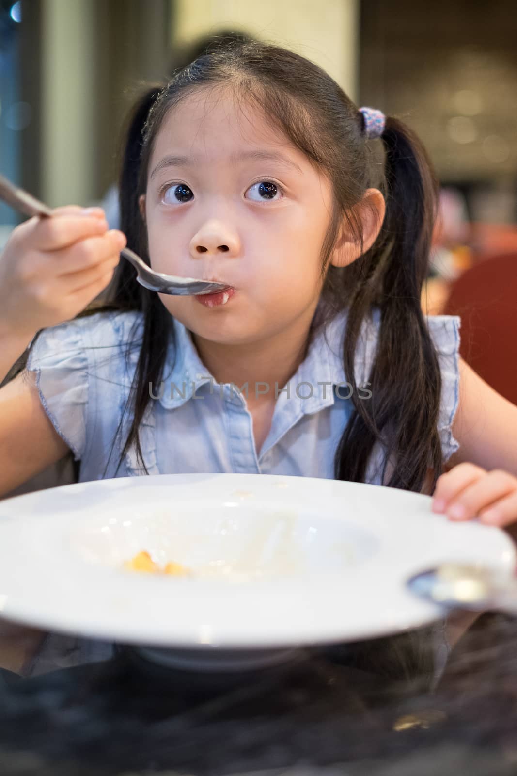 Hungry Asian child, girl, sipping soup from spoon.