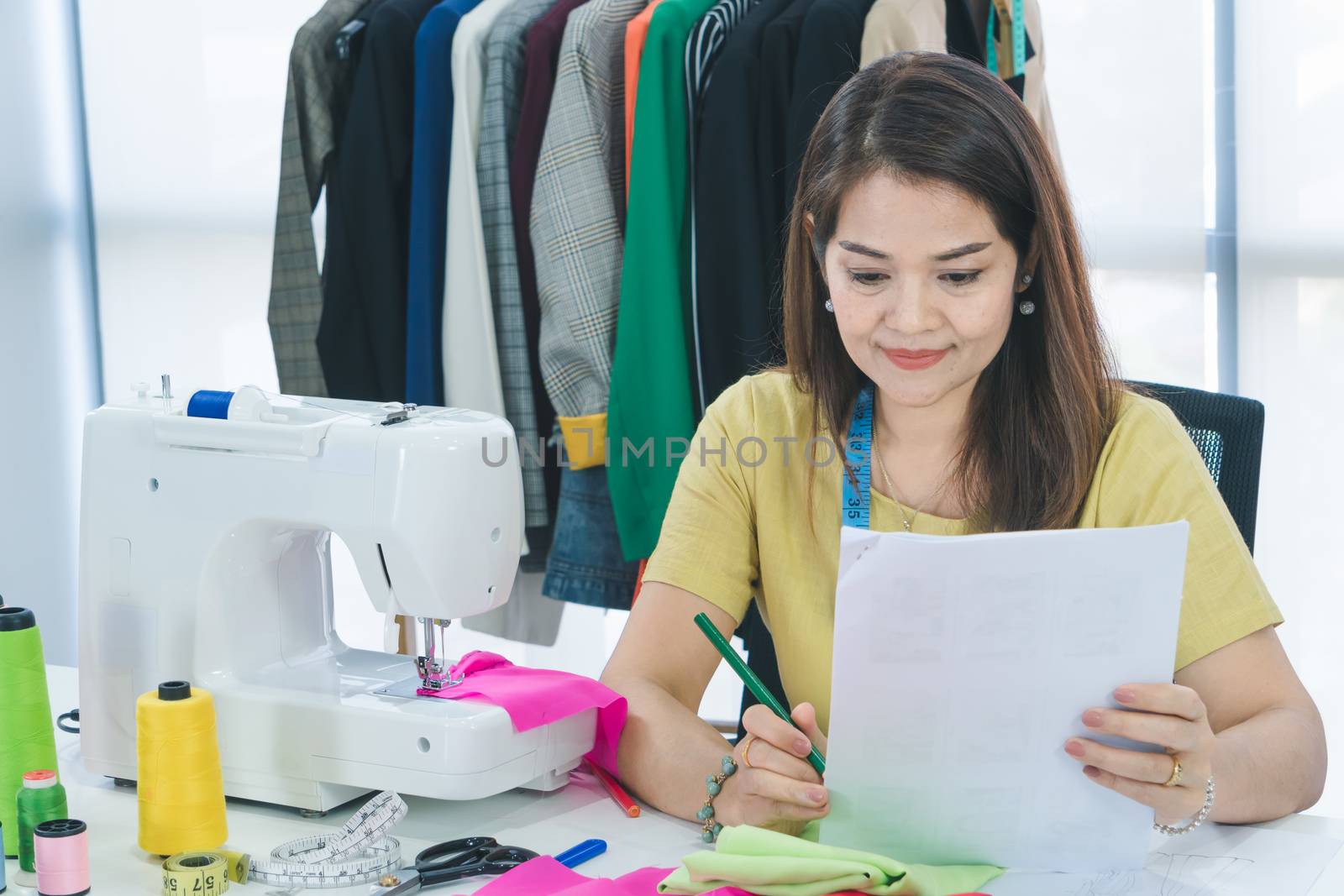 An Asian female fashion designer is working and smiling happily. Small businesses work from home.