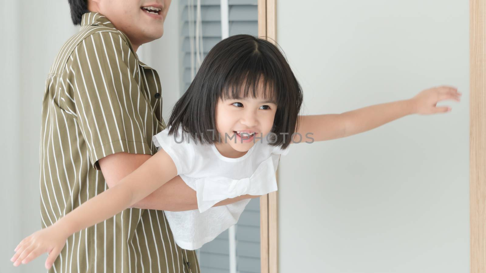 An Asian family with a cute father and daughter. They were having fun playing in the bedroom. The father picked up his daughter and then became obsessed with it.