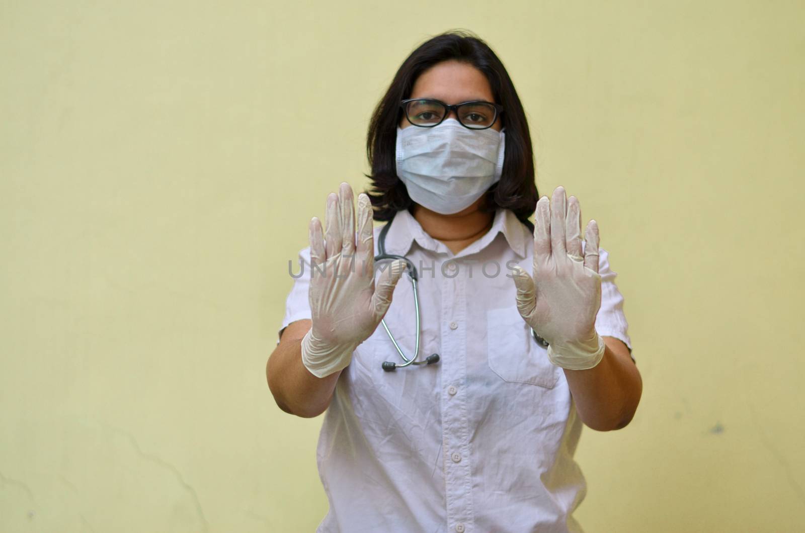 Portrait of young medical healthcare female worker showing her hands out & wearing surgical face mask to protect from Corona Virus (COVID-19) pandemic against yellow background.Concept Ready to fight