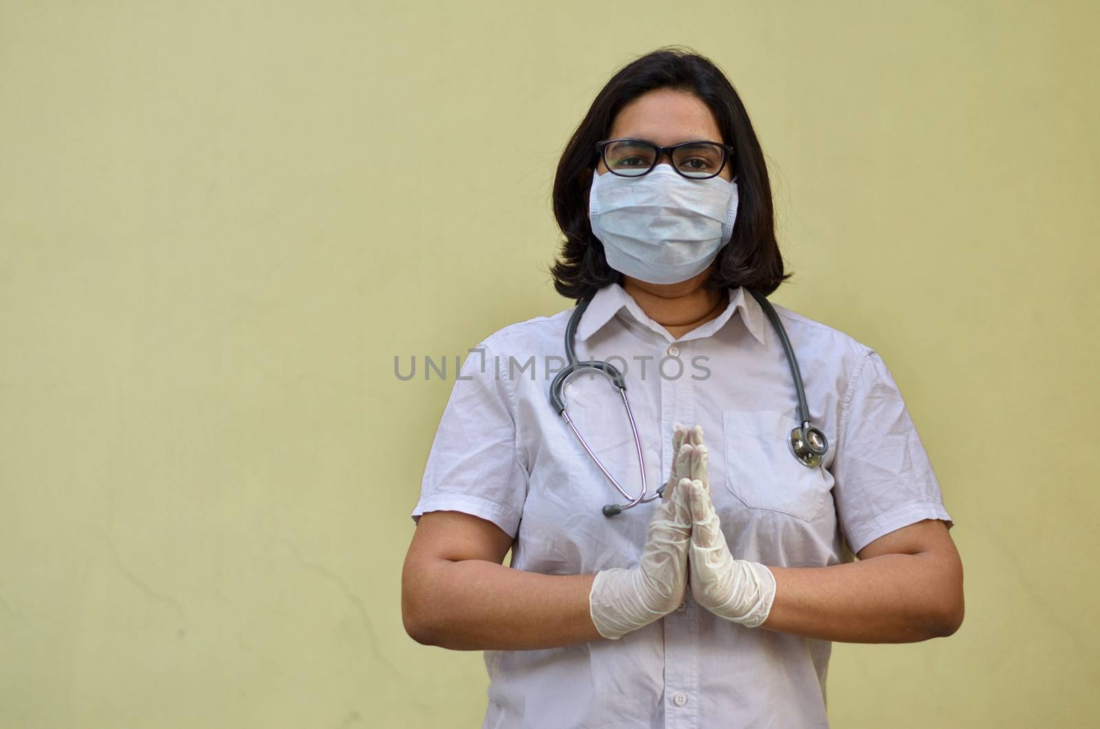 Portrait of young medical healthcare female worker wearing surgical face mask to protect herself from Corona Virus (COVID-19) pandemic against yellow background. Concept : Getting ready to fight