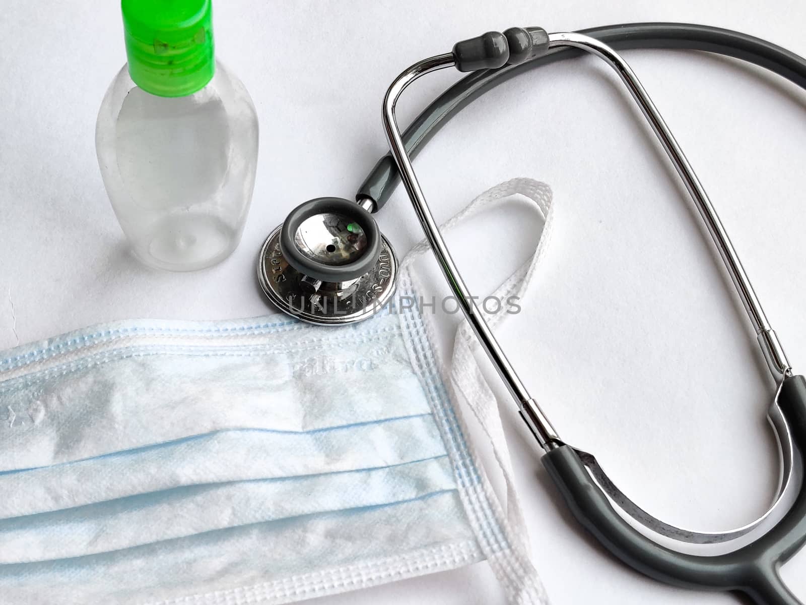 White breathable surgical face mask, sanitizer and stethoscope on a white background denoting doctor's Corona virus (Covid-19) safety kit to reduce the rate of spread of infections