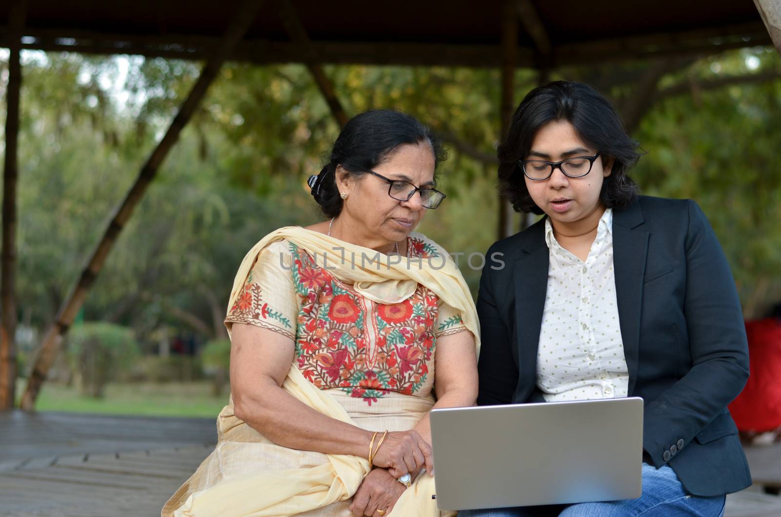 Young Indian woman helping her old retired mother on a laptop sitting in a park in New Delhi, India. Concept - Digital literacy / Education, Mother's Day