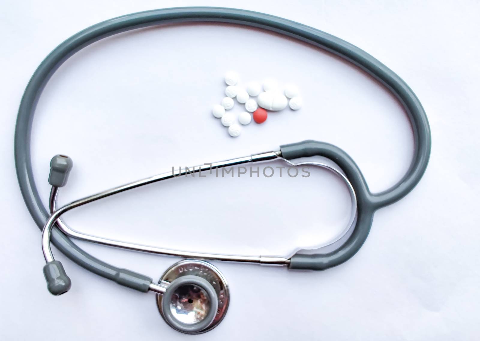 Pills spilled out of a plastic bottle with a stethoscope in the frame and isolated on white background. Top view with copy space. Medicine concept