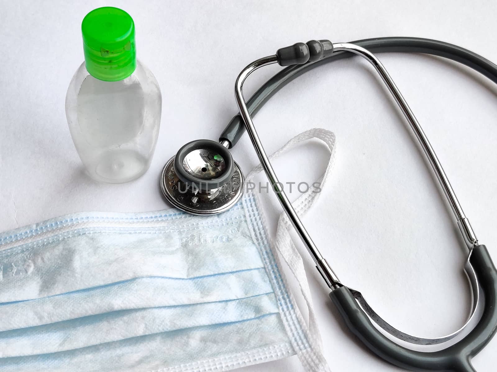 White breathable surgical face mask, sanitizer and stethoscope on a white background denoting doctor's Corona virus (Covid-19) safety kit to reduce the rate of spread of infections