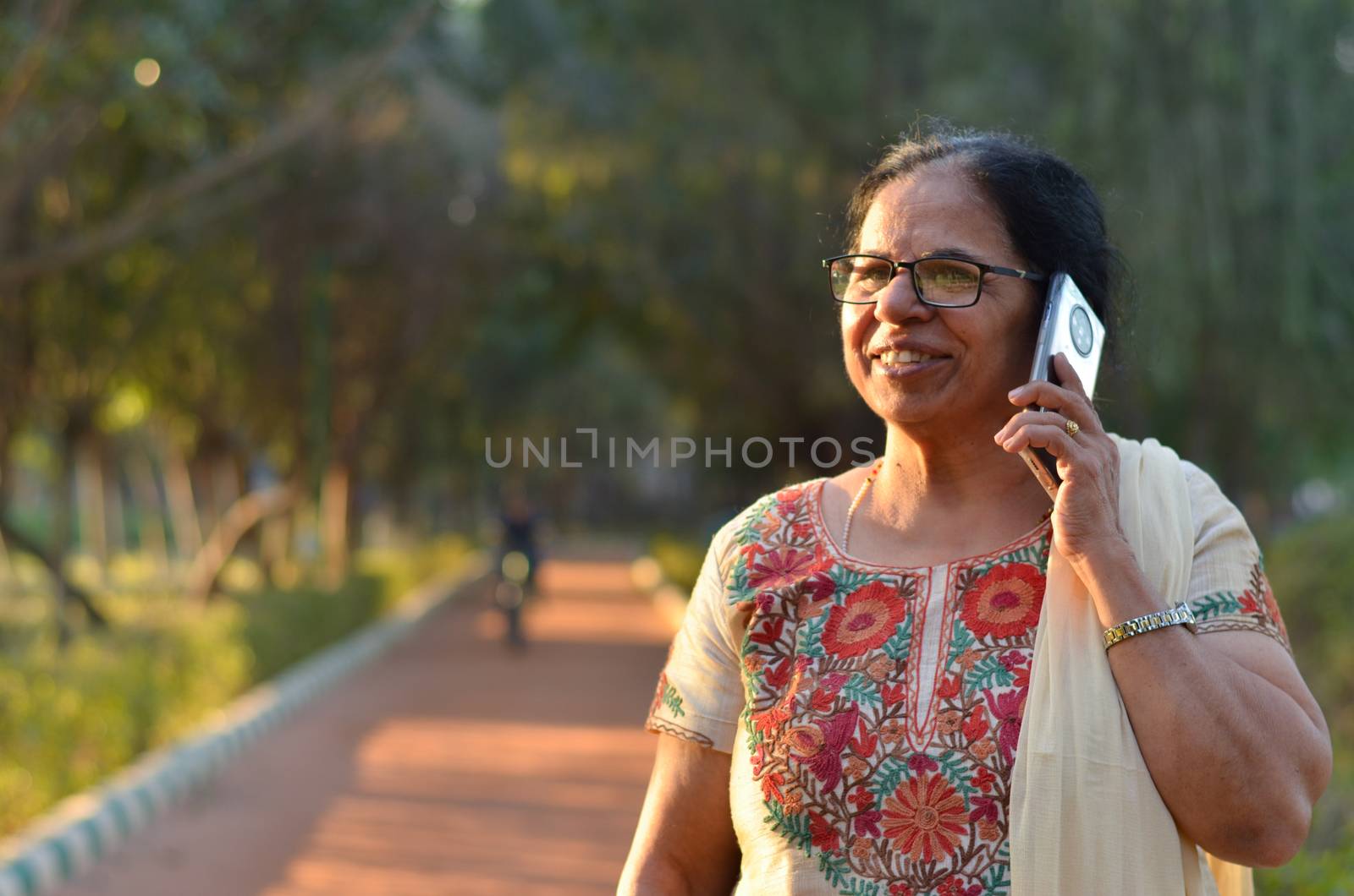 Senior Indian woman laughing and speaking on mobile smart phone in a park wearing off white salwar kamiz. Concept - Digital literacy in India for senior citizens