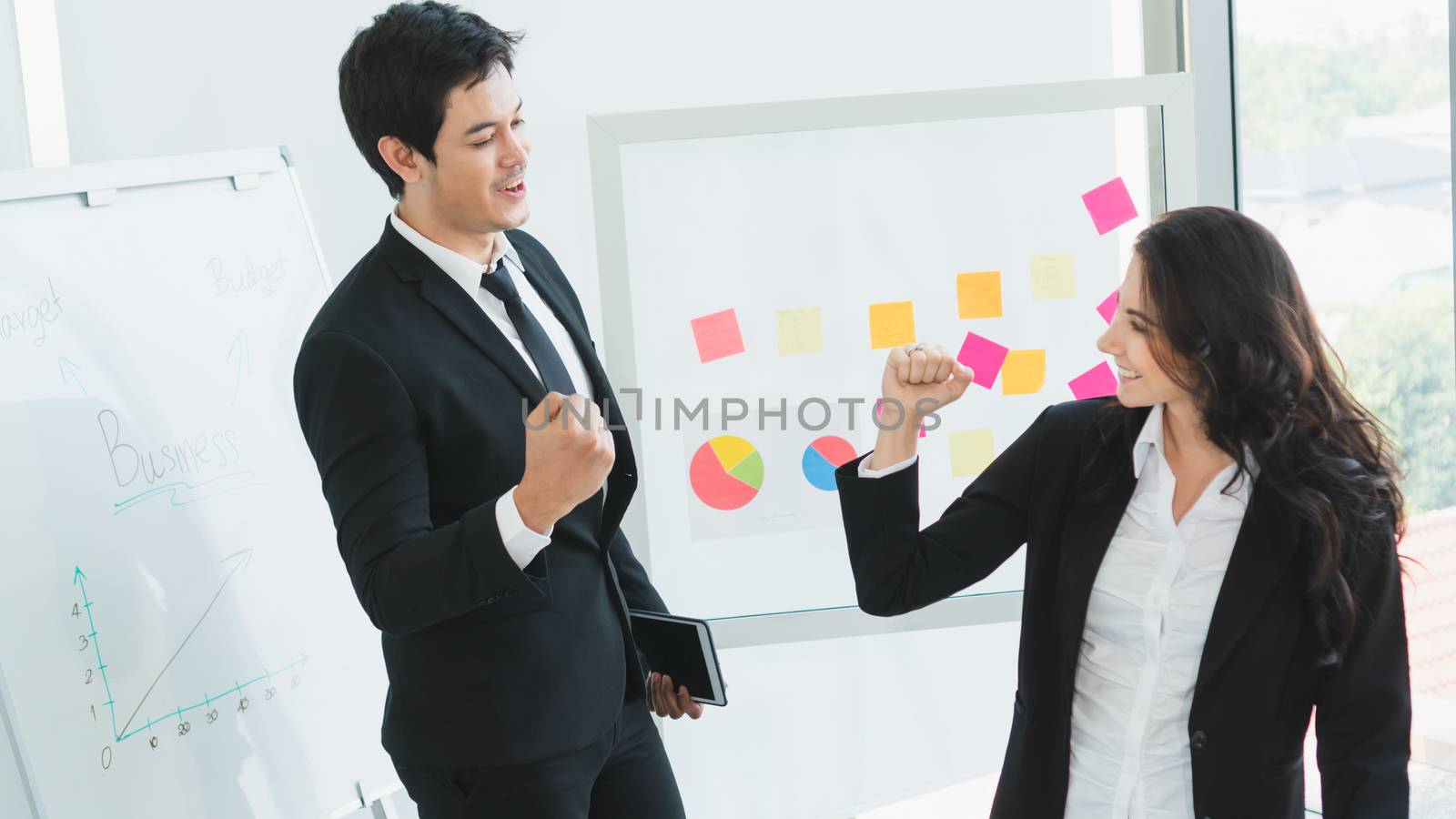 A photograph of a young Asian businessman and a Caucasian businesswoman wearing a black suit working together in an office.