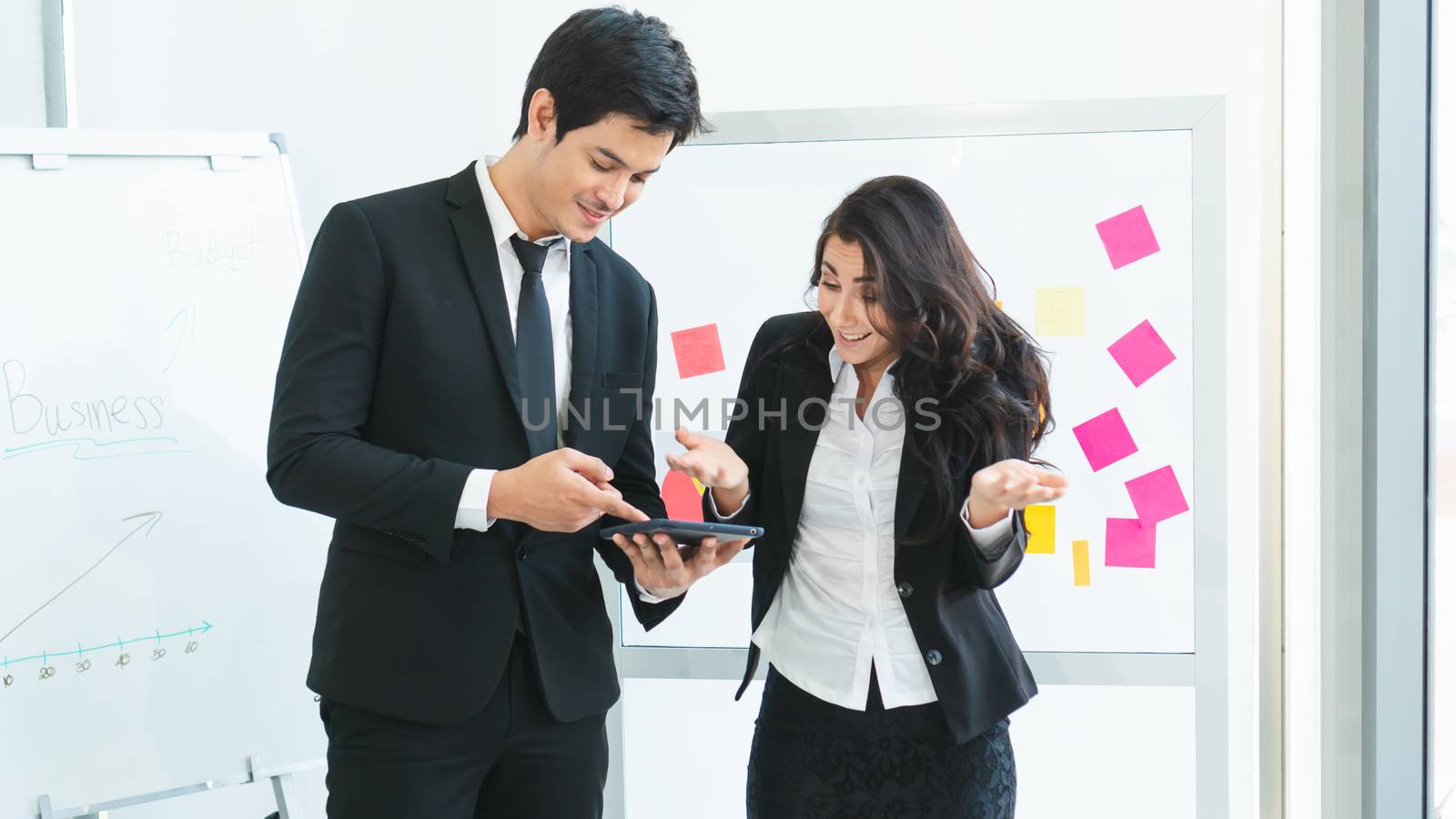 A photograph of a young Asian businessman and a Caucasian businesswoman wearing a black suit working together in an office.