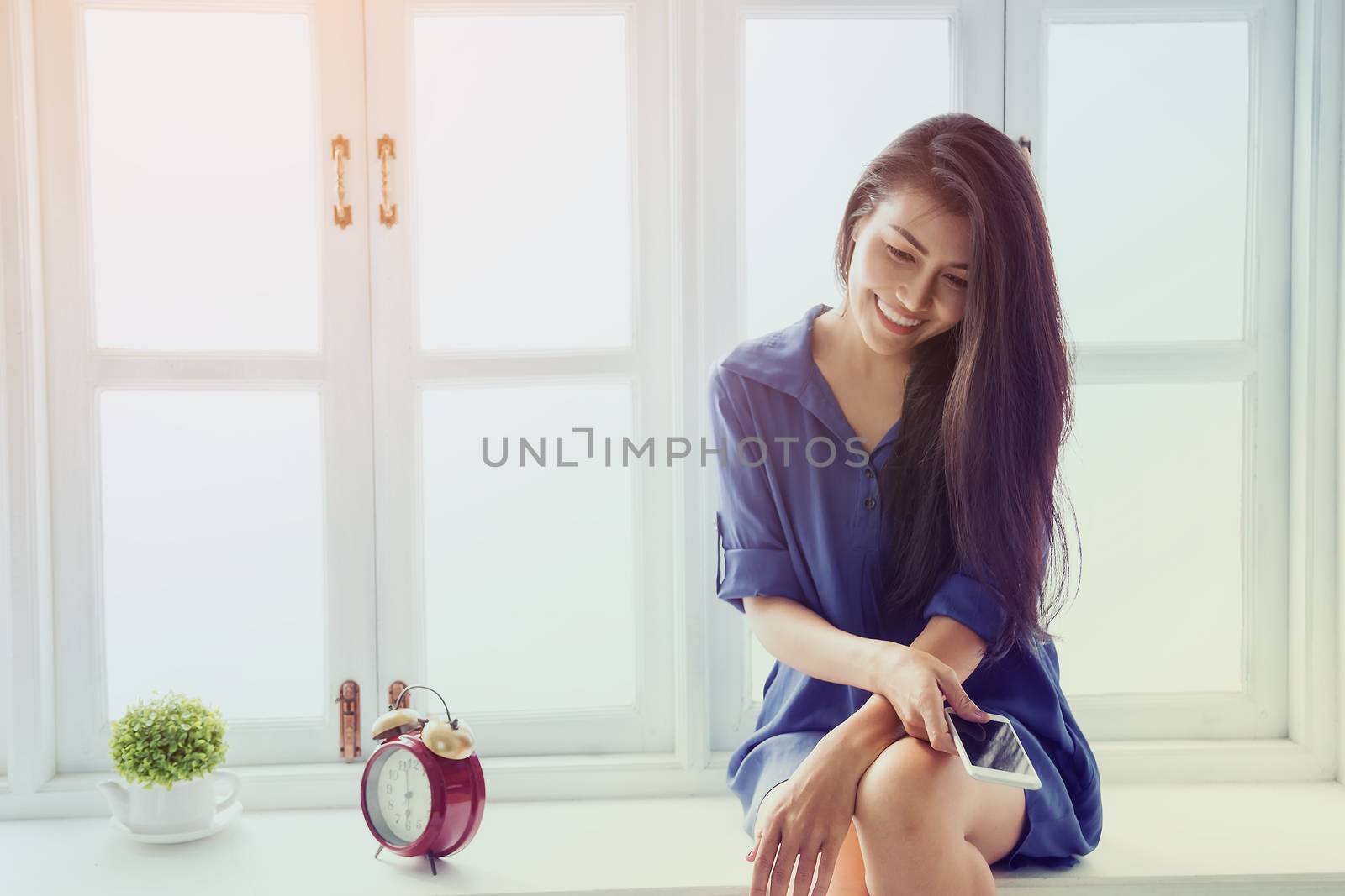 Picture of a beautiful girl who is awake, sitting, relaxing, drinking coffee, playing mobile and reading a book by the window.