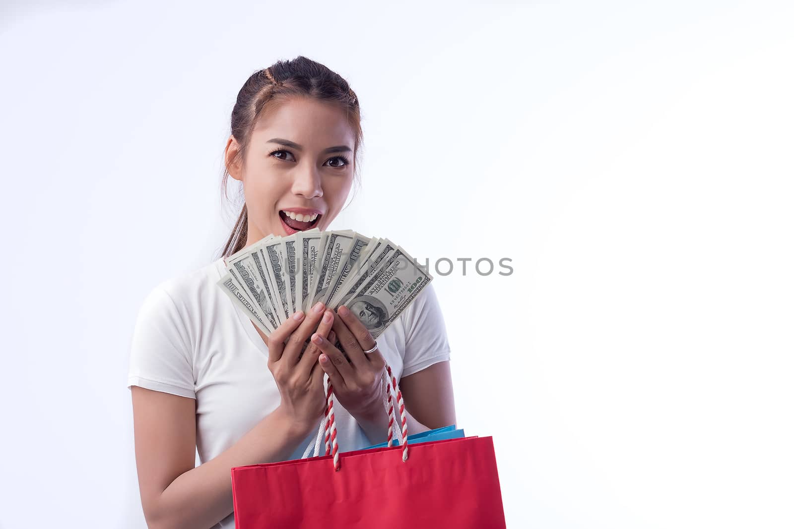 Picture of a beautiful black haired girl in a summer dress, holding a dollar bill with a shopping bag, and looking at the camera through a white background.