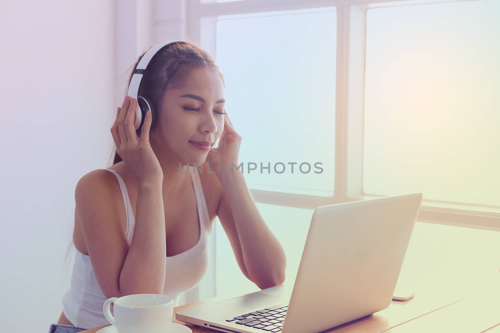 Picture of a beautiful girl in a white dress, sitting by the coffee and listening to music happily by the window.