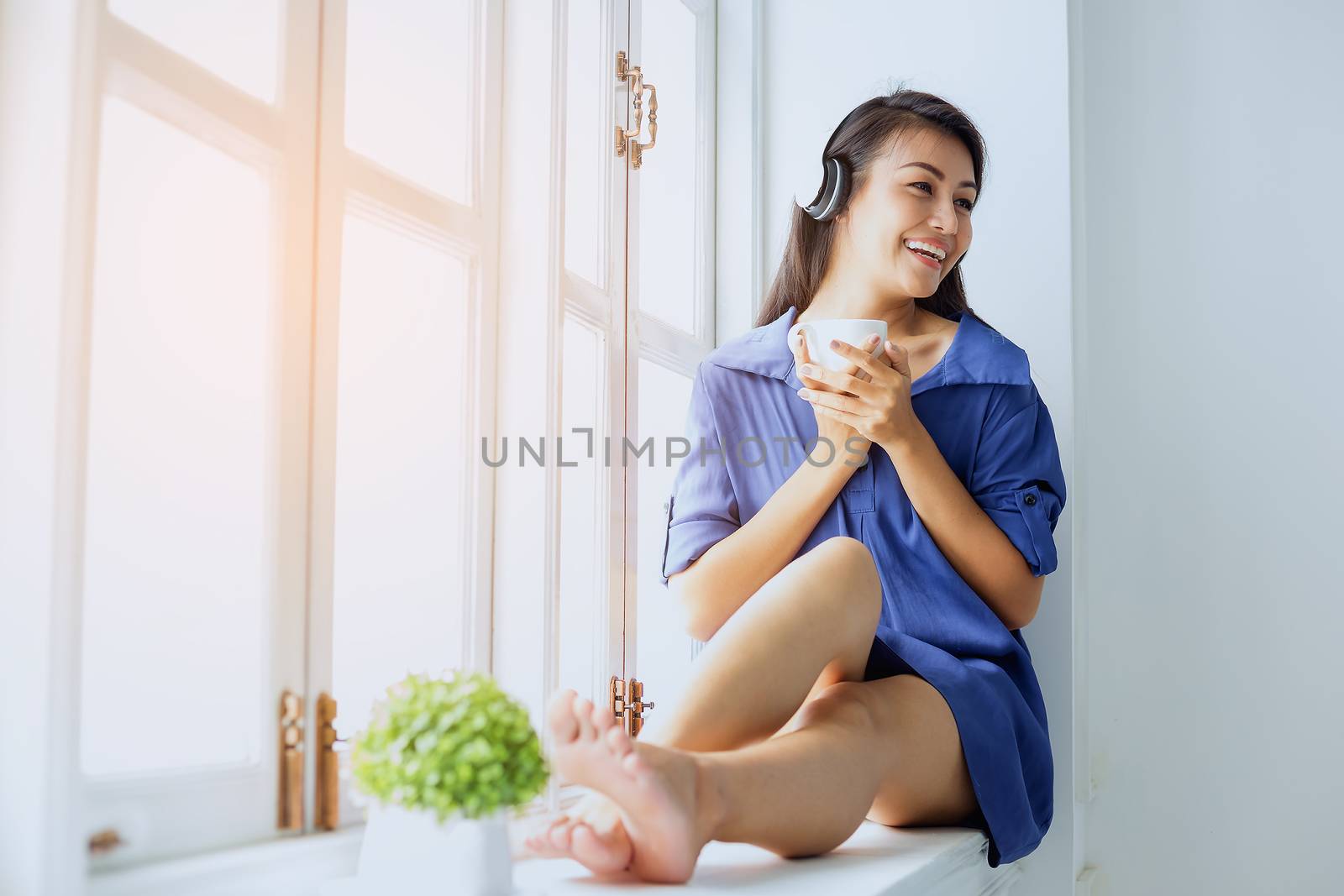 Picture of a beautiful girl who is awake, sitting, relaxing, drinking coffee, playing mobile and reading a book by the window.