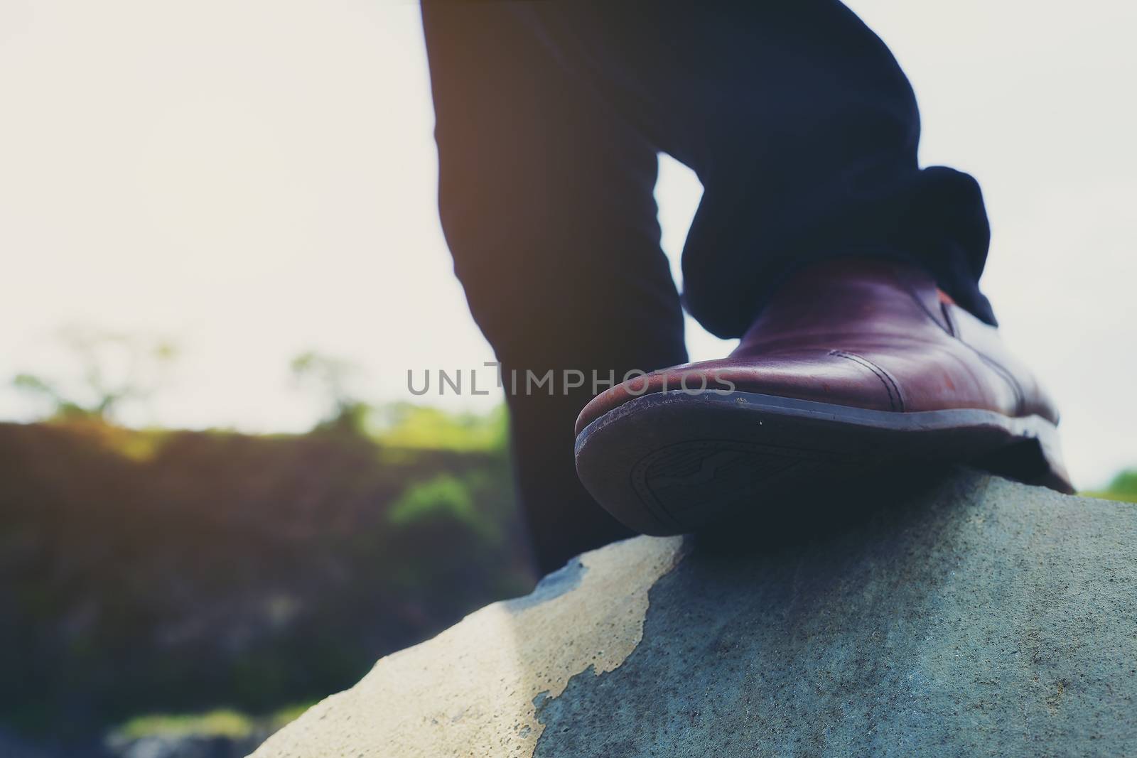 Photo of hipster men's fashion shoes in brown suede shoes walking on rocks in bright weather.