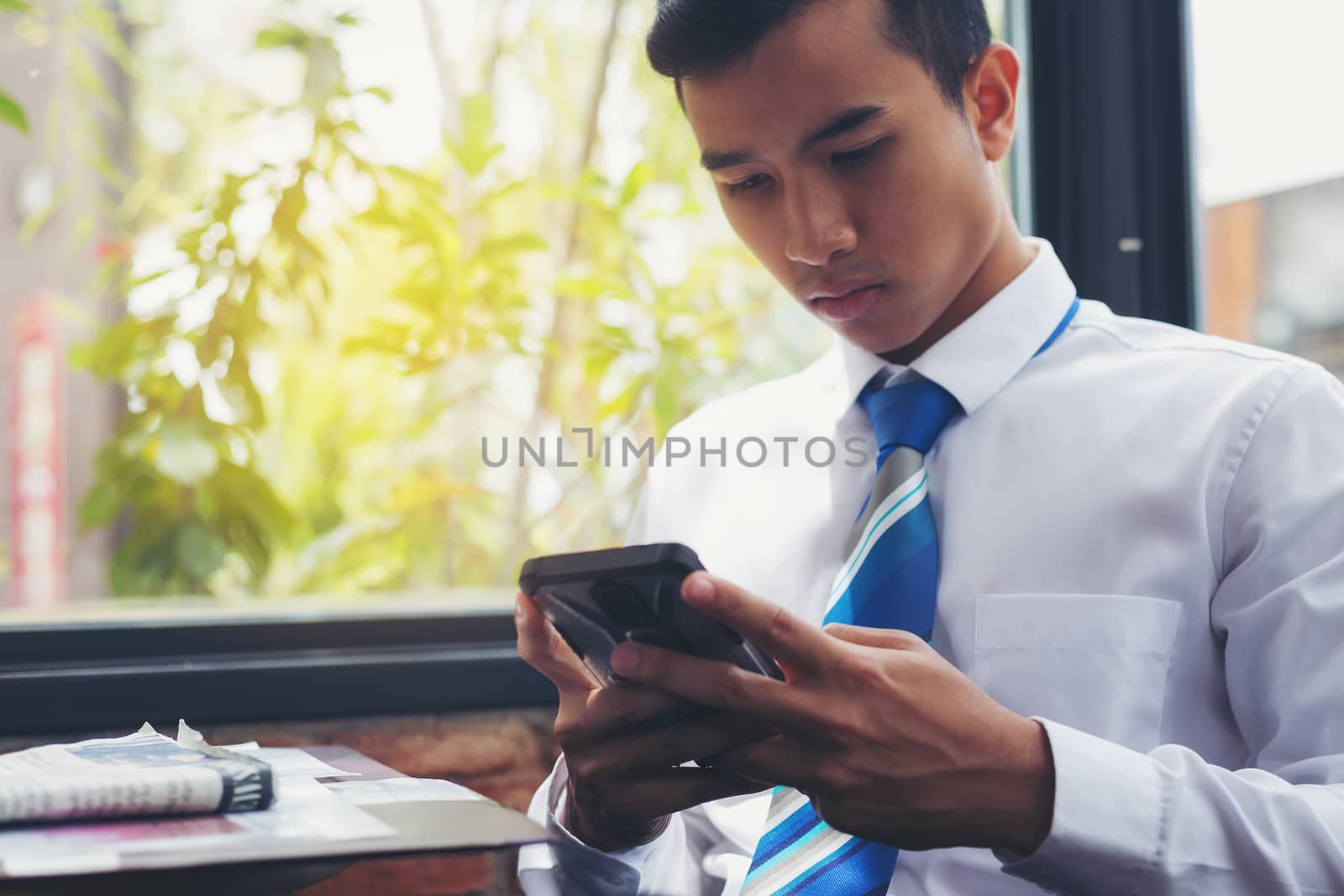 A handsome businessman reading a text from a mobile phone while sitting in a coffee shop.