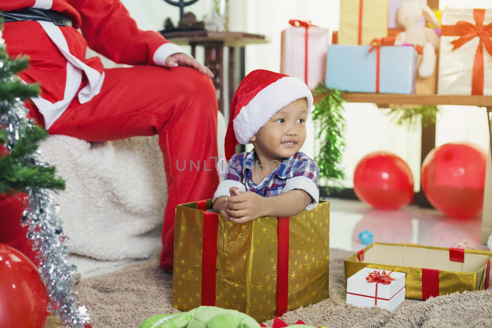 Santa Claus opens a gift box with little boy sitting in a box.