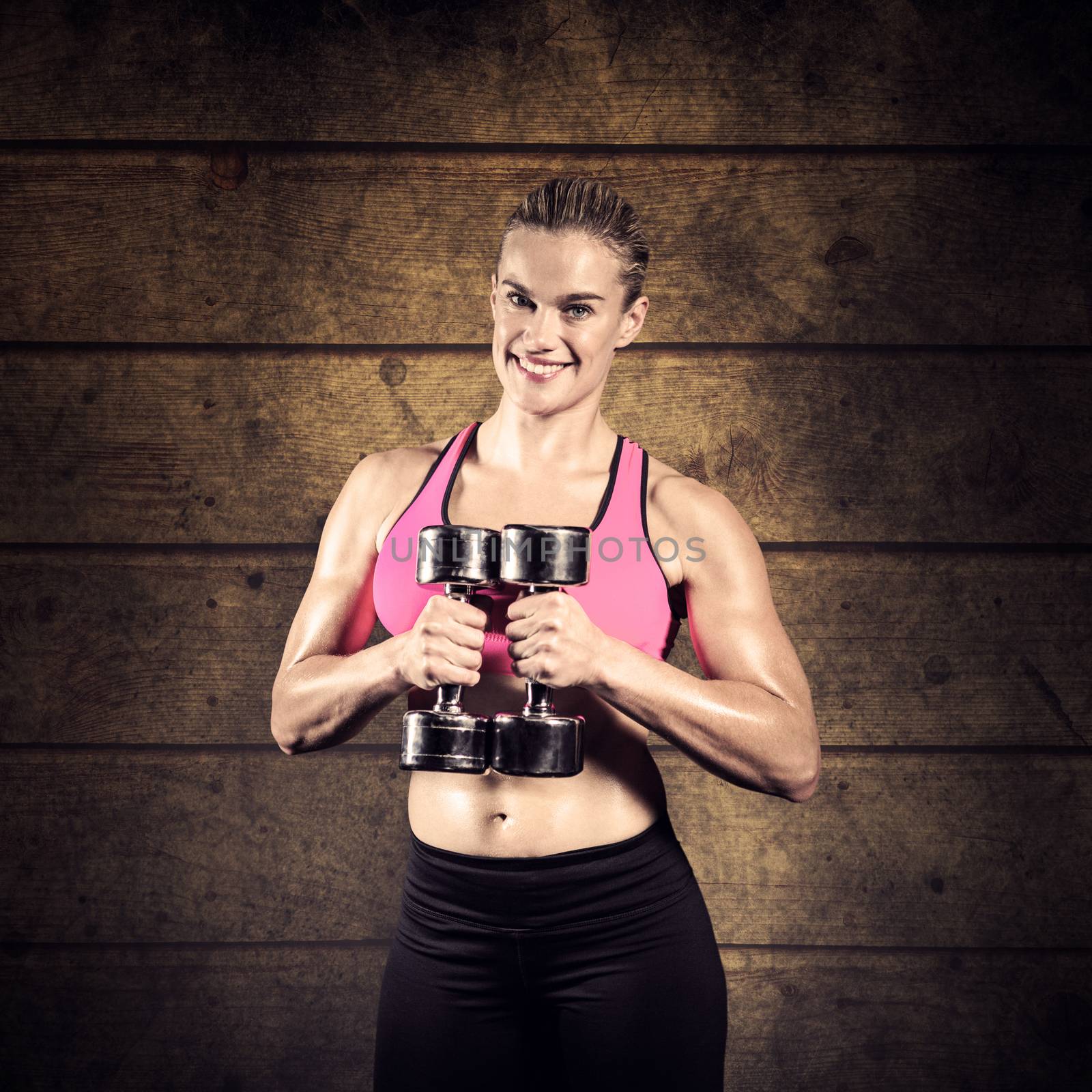 Muscular woman lifting heavy dumbbells against dark fence