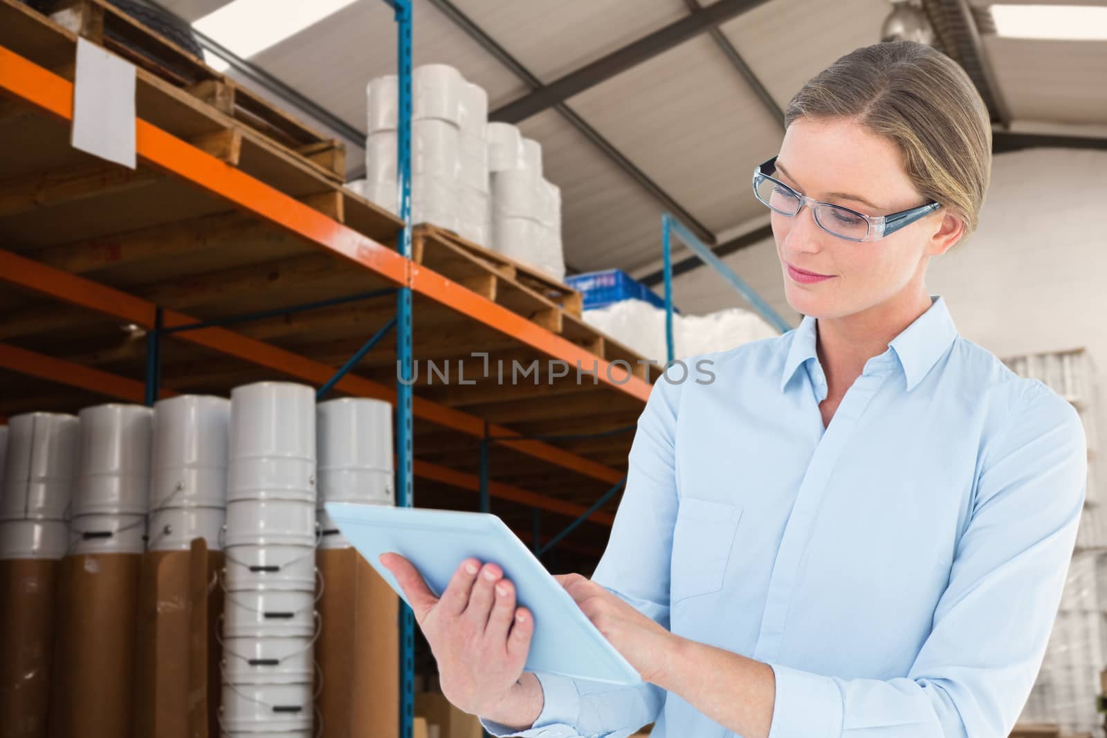 Businesswoman using tablet pc  against warehouse manager checking her list on clipboard