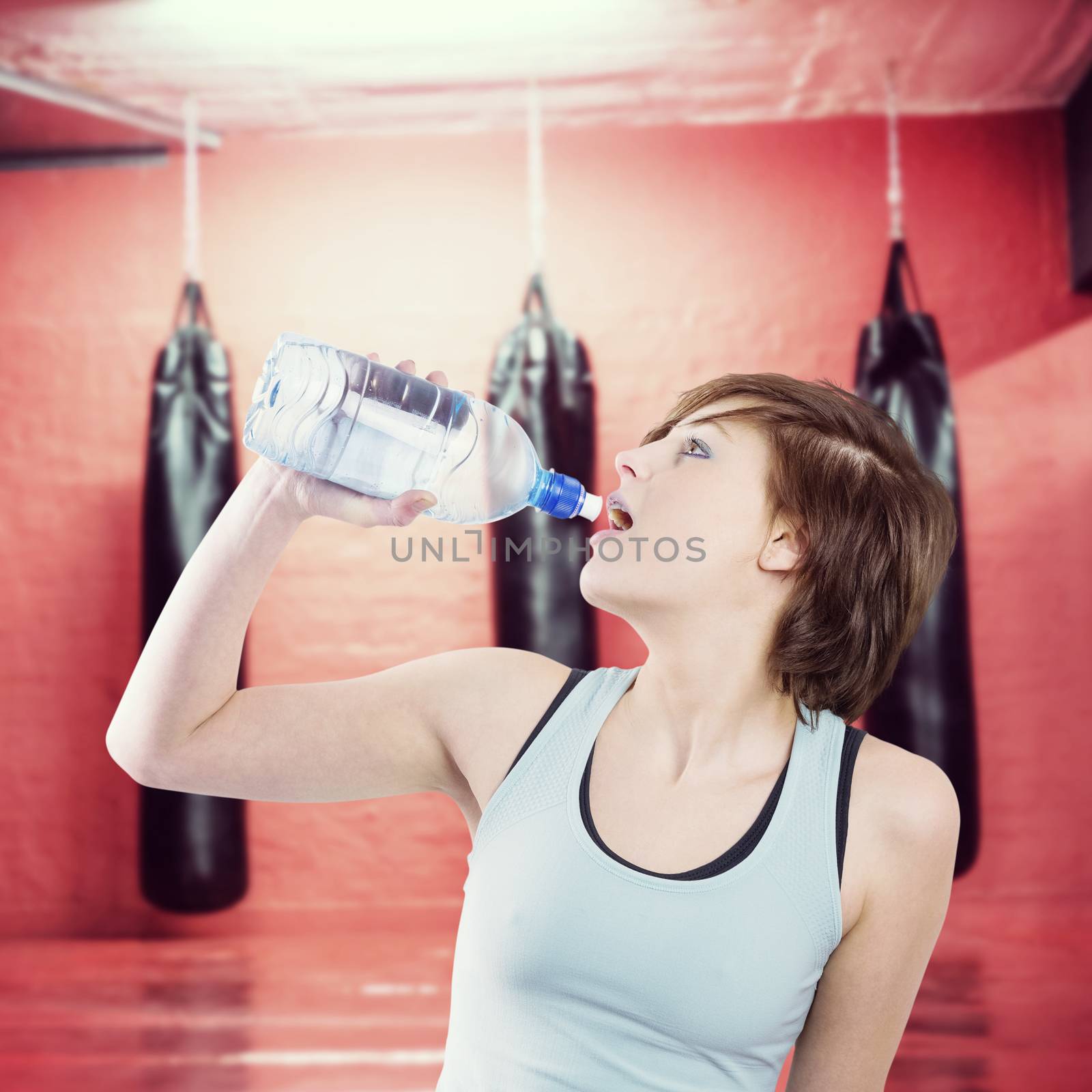 Pretty brunette drinking water against punching bags in red boxing area