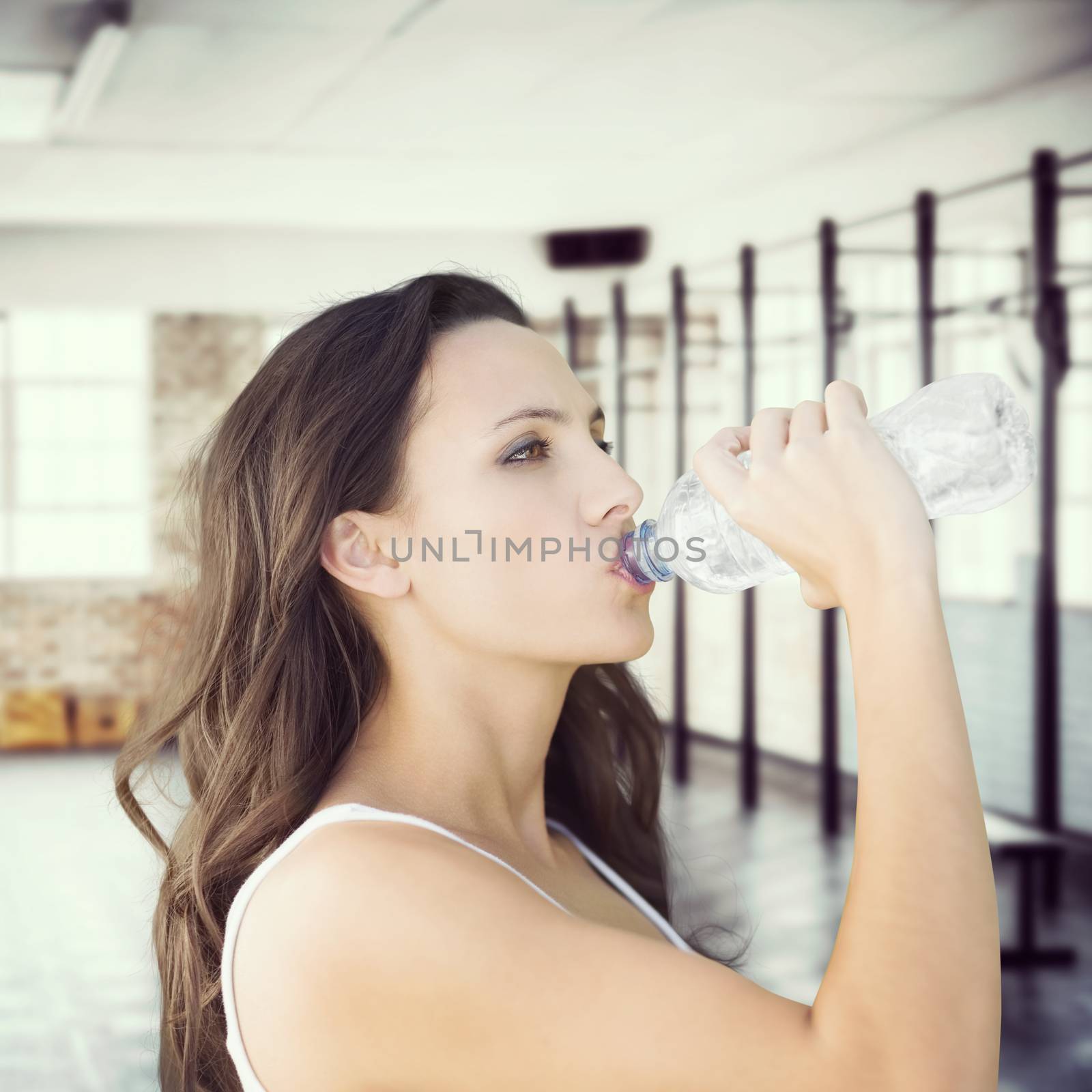 Beautiful woman drinking water from bottle against gym