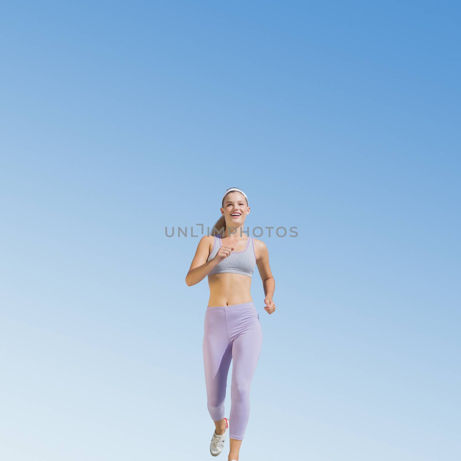 Sporty blonde jogging towards camera against blue sky