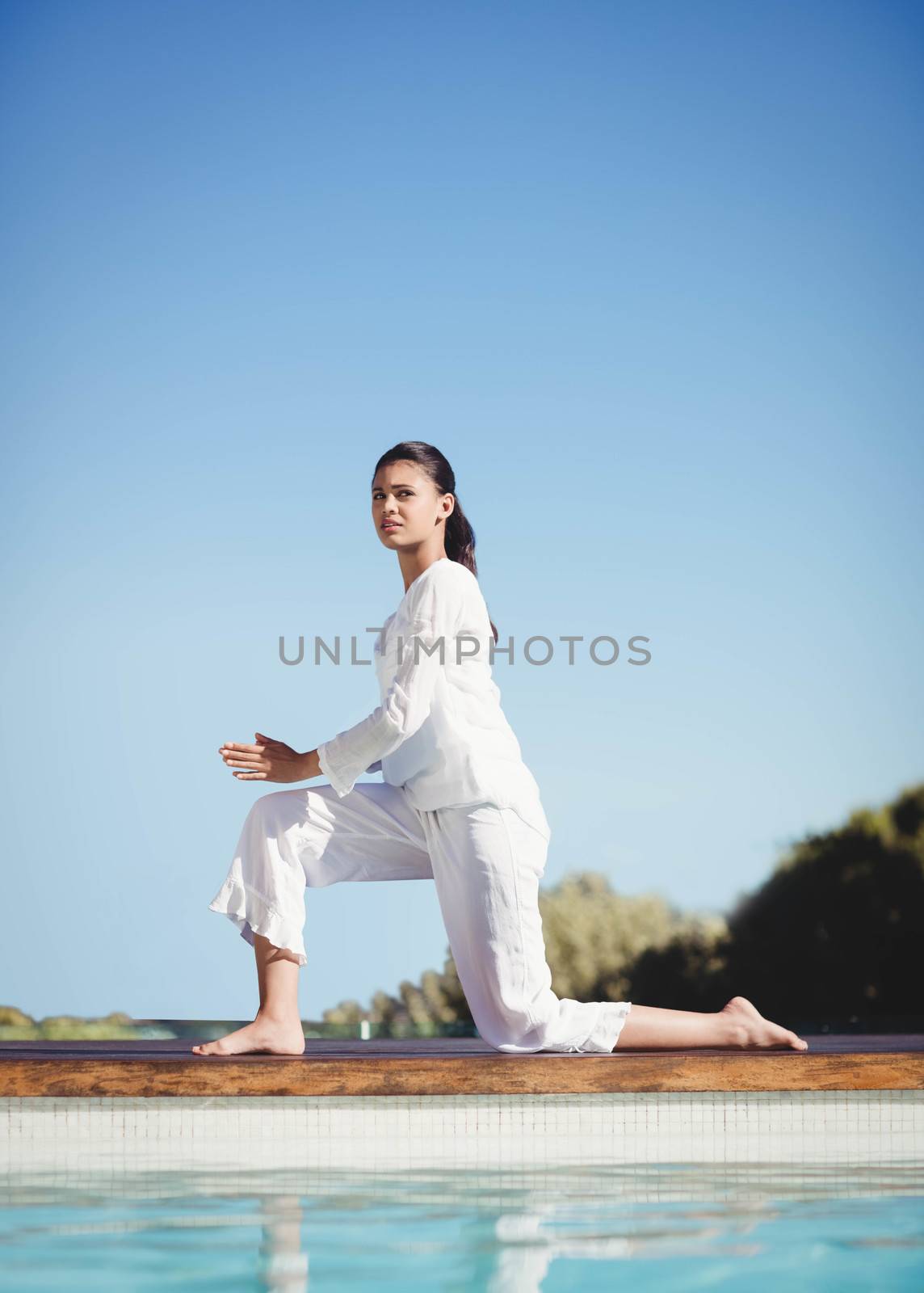 Calm brunette doing yoga by the pool