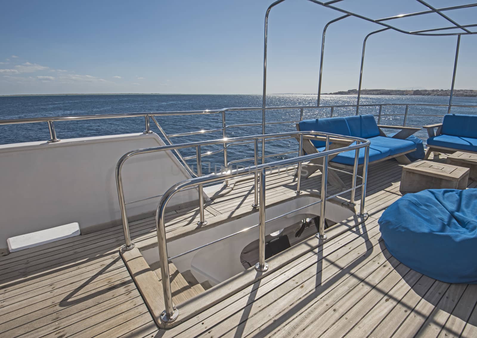 Stern teak sundeck of a large luxury motor yacht with chairs sofa table and tropical sea view background