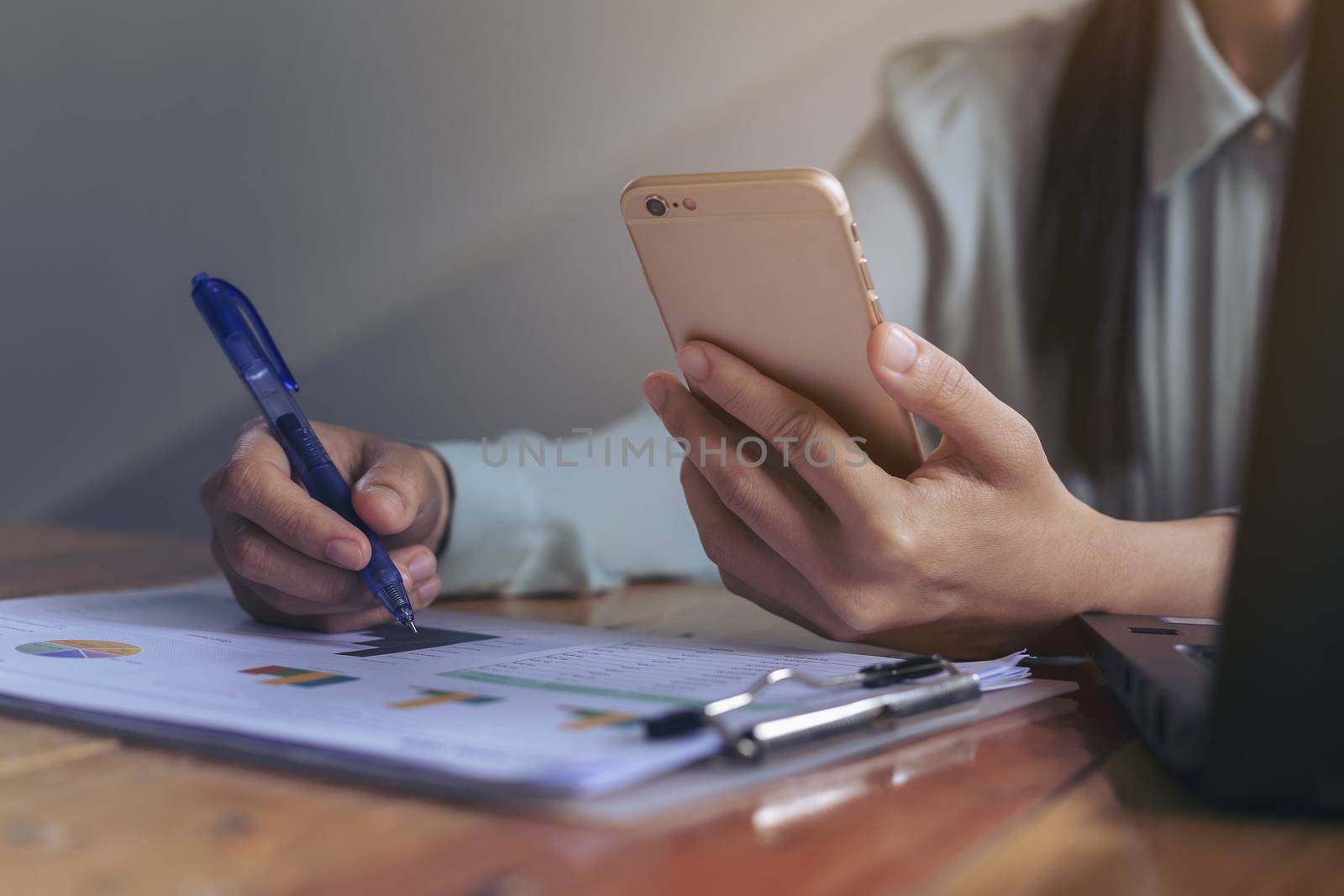 Beautiful young businesswoman is searching for information with a mobile phone. And look at the chart from the paper to make a decision.