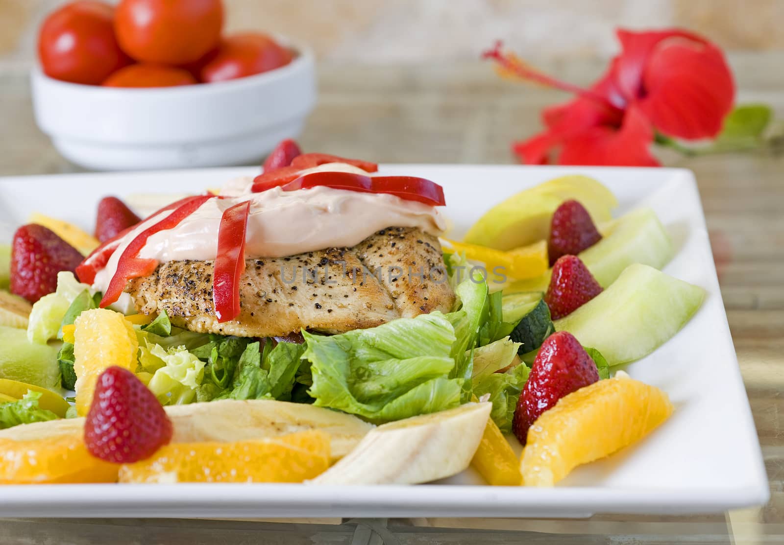 Chicken salad on a white plate with dressing and a fresh fruit garnish