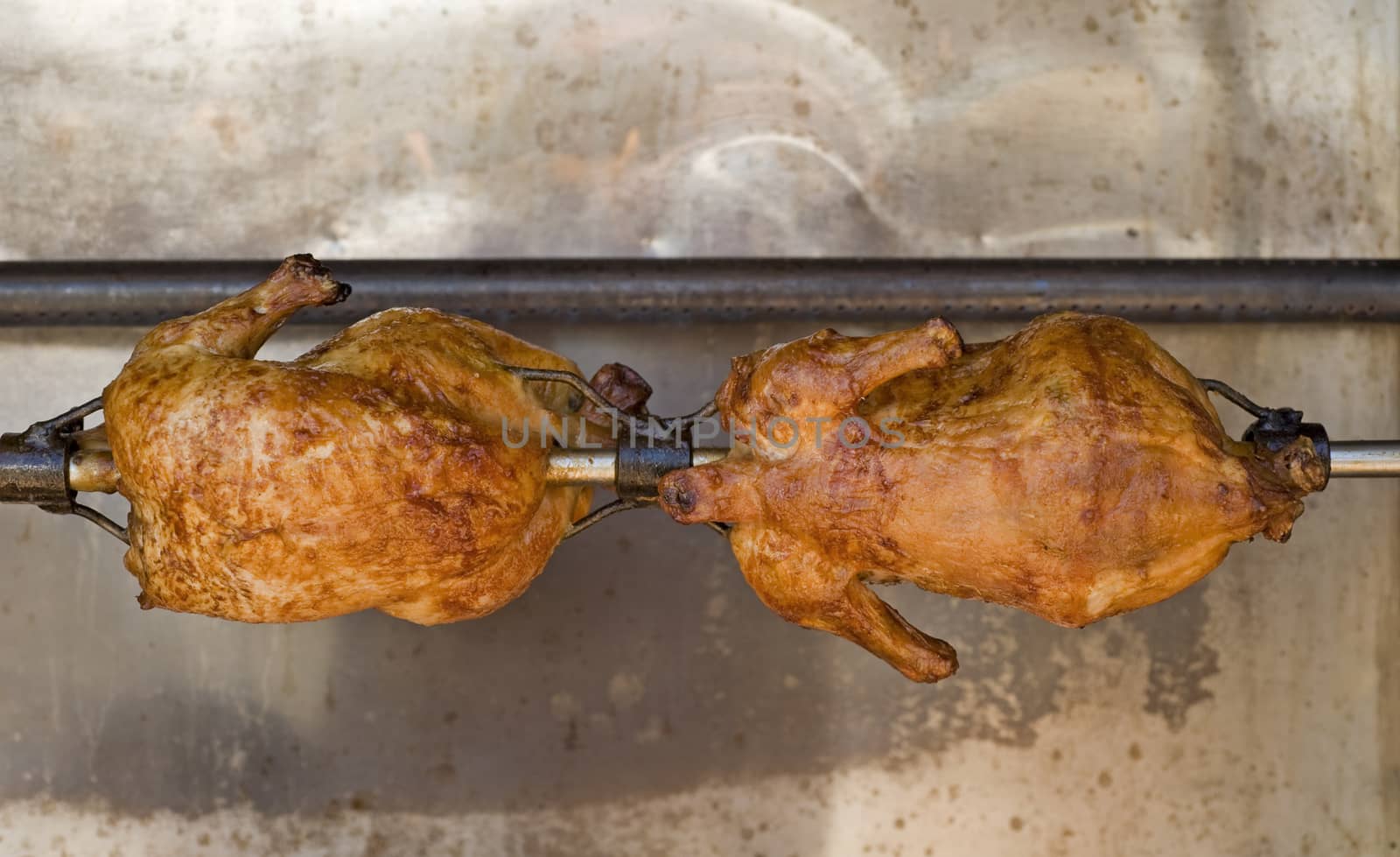 Two whole chickens roasting on a spit with a open flame