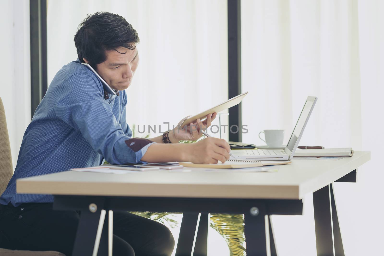 Busy businessman under stress due to excessive work. Serious focused businessman working on laptop computer online and many mobile phones.