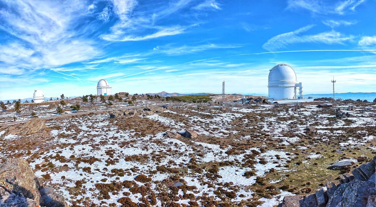 Panoramic of Calar Alto Observatory at the snowy mountain top in Almeria, Andalusia, Spain, 2019. Sky passing through against the domes