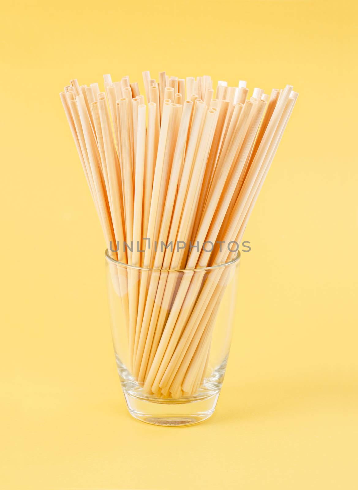 Wheat Straws for drinking water natural eco friendly renewable in glass on yellow background.