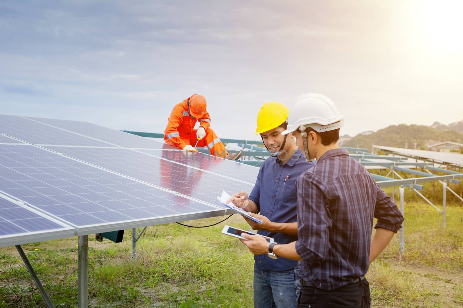 Engineers and workers in uniform and installs solid solar panels on a metal base in a solar farm.