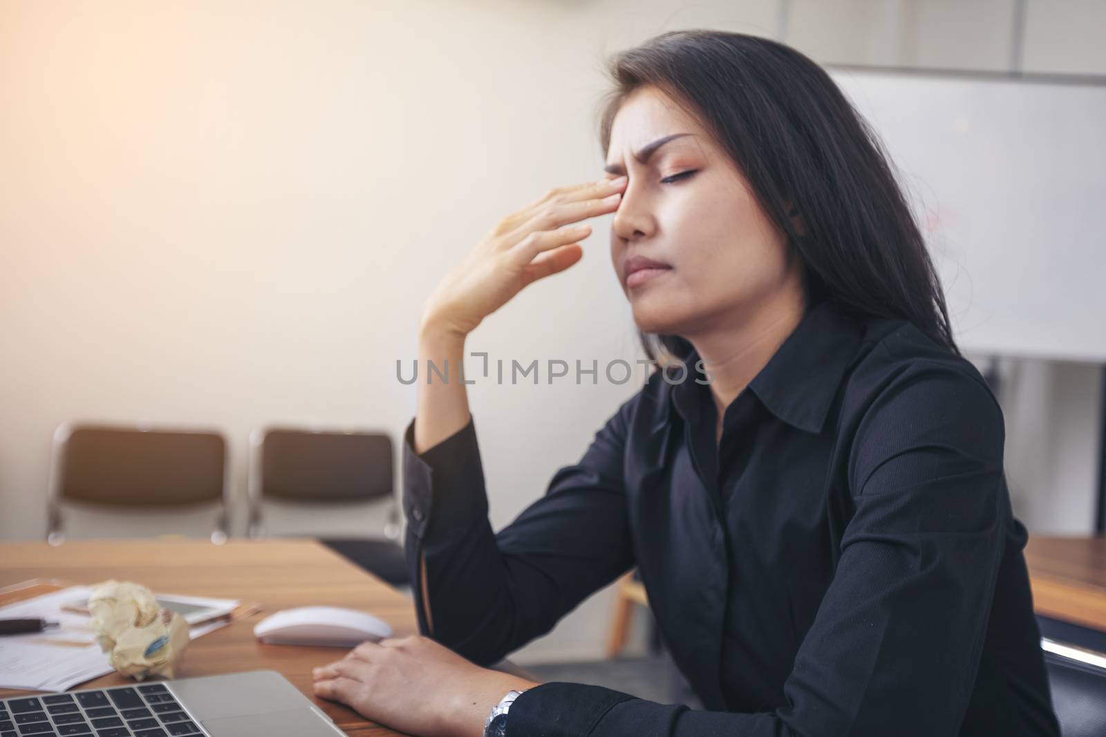 Businesswoman suffering migraines at job working on line with a laptop sitting in a desktop at office. Tired businesswoman suffering of headache. 