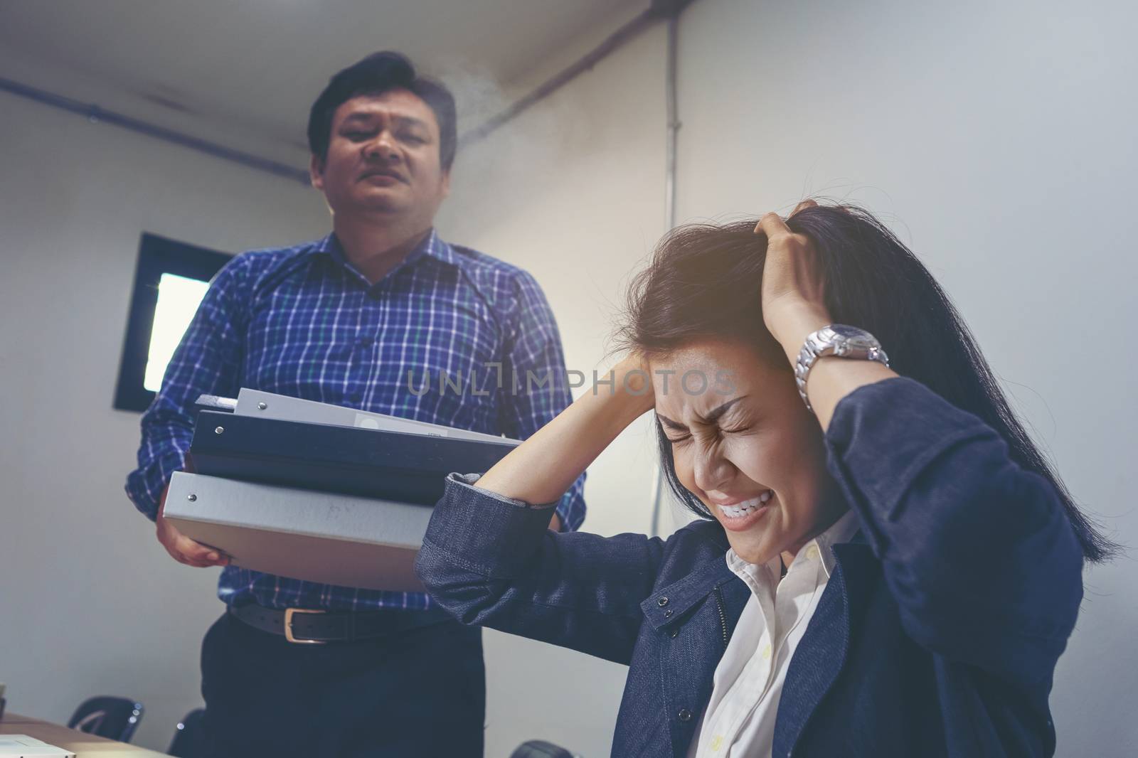 Deadline stress concept - furious business woman sitting at desk in office and shouting while holding hands on head with stress from hard work