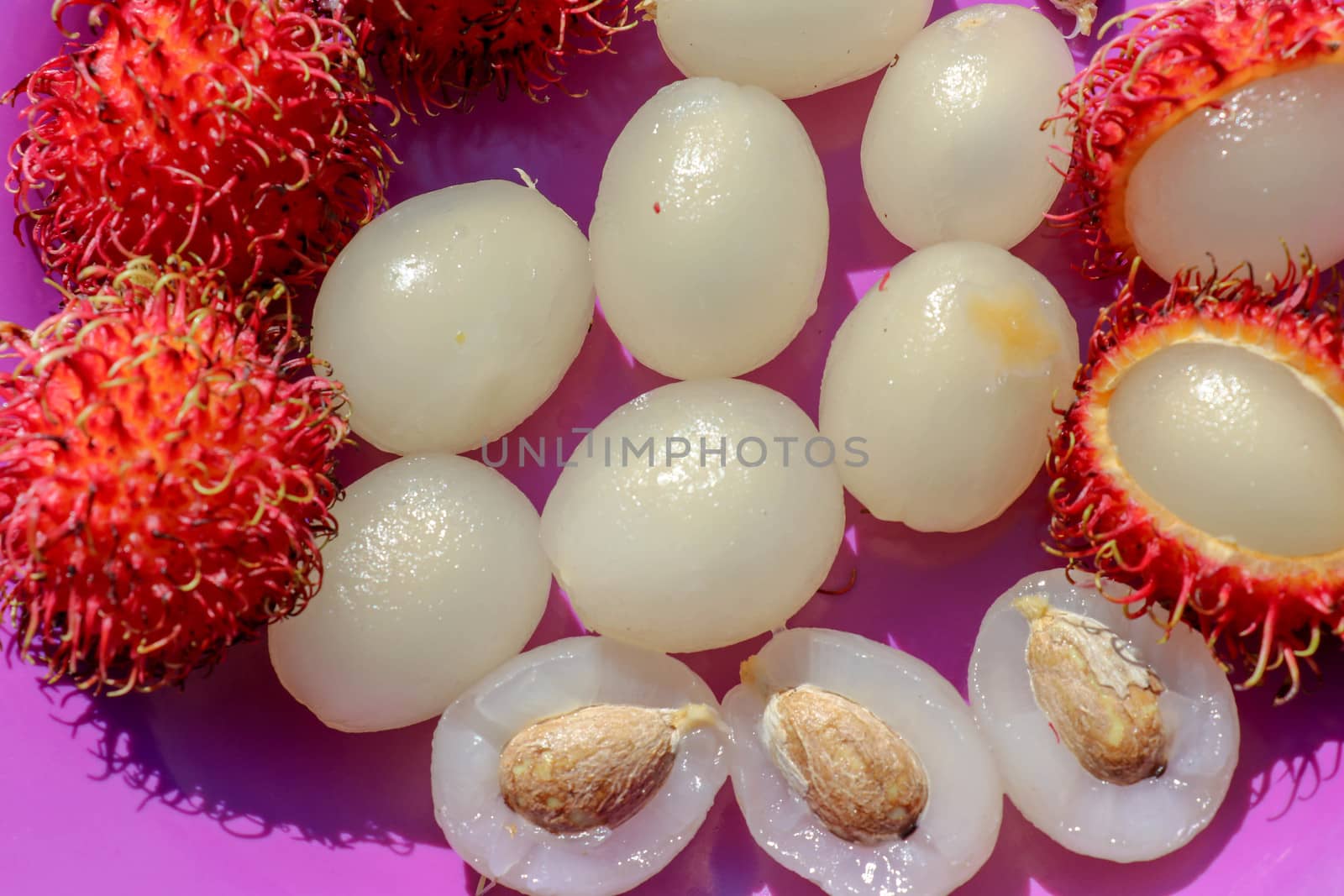 Close up of rambutan, whole and peeled fruits. Top view Healthy fruits on purple background. Ready to Eat Sweet Bali Fruit. Fruit is rounded oval single-seeded berry covered with fleshy pliable spines