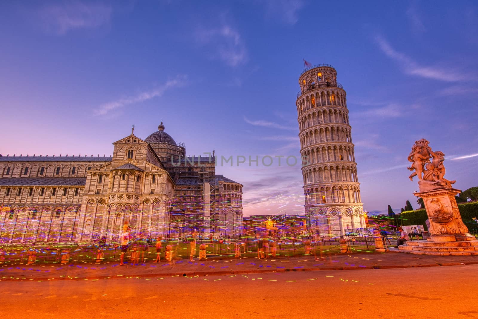 Pisa, Italy - July 8, 2018: Piazza dei miracoli, with the Basilica and the Leaning Tower, Pisa, Italy. Colored lights of street vendors