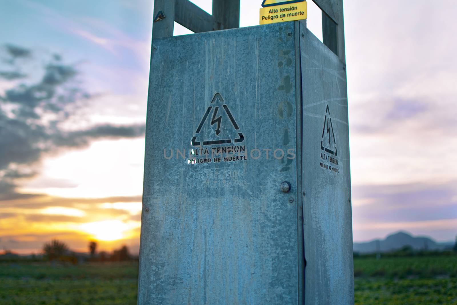 High voltate sign in the base of an electric tower at sunset. Cell tower, electricity, cables. Written high voltate, death danger in the text