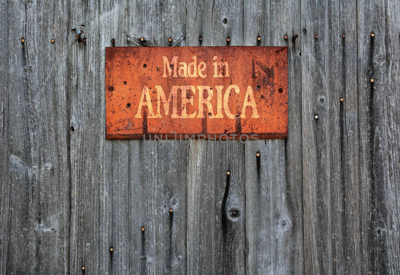 Rusty metal sign on wooden wall with the phrase: Made in America.