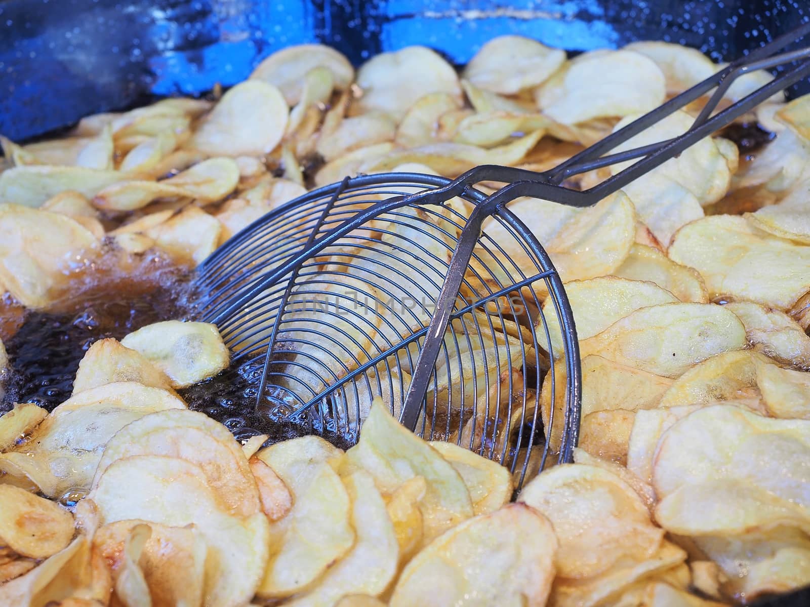 Frying chips in a black pan with a lot of boiling oil in a restaurant.