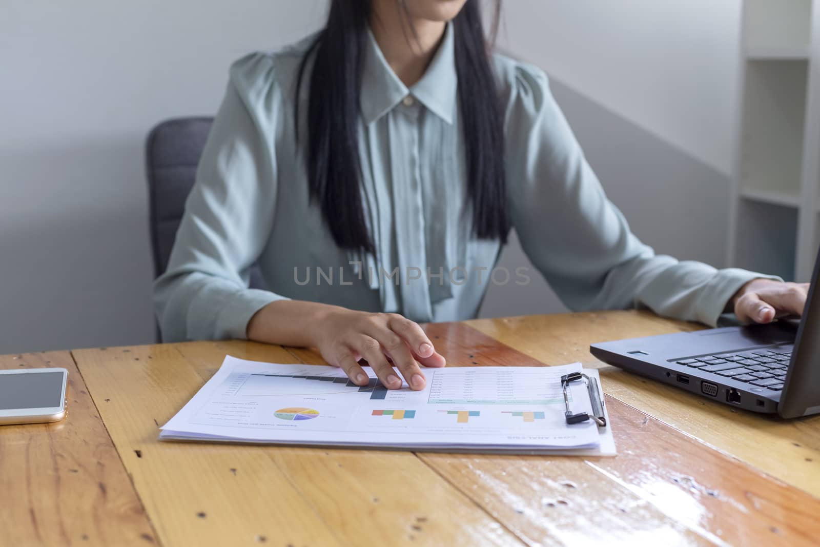 Beautiful young businesswoman doing some paperwork while sitting at office desk in front of computer.