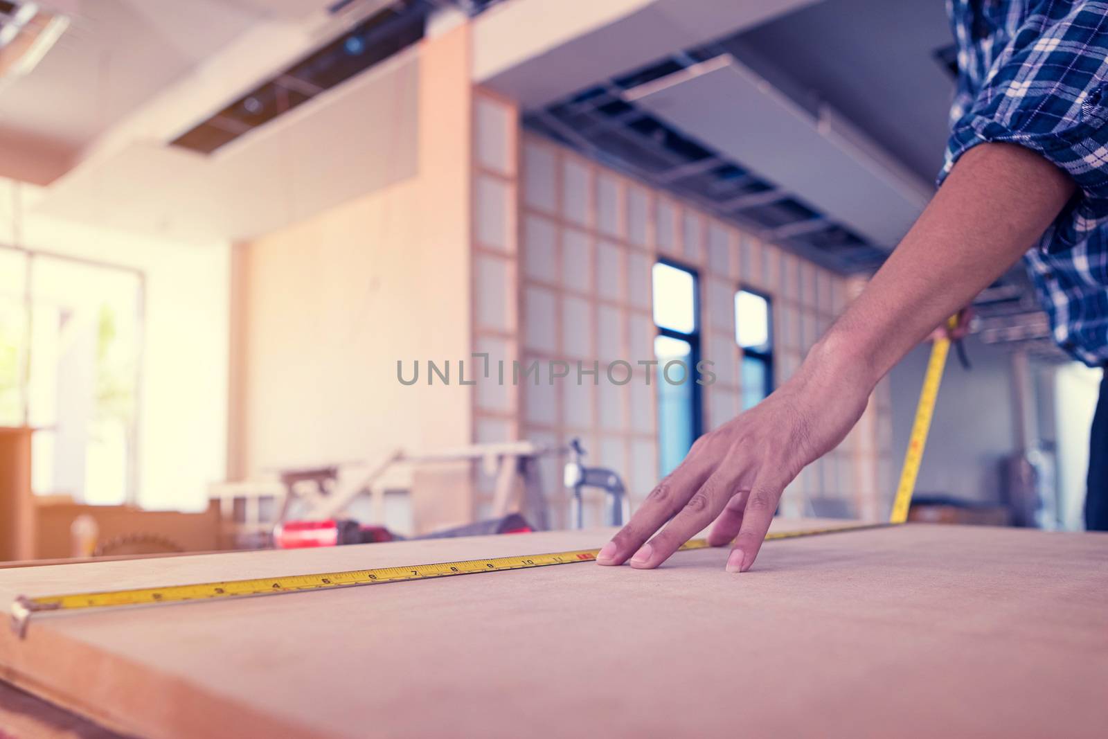 The carpenter is using a tool to measure the size of the wood for use in his work.