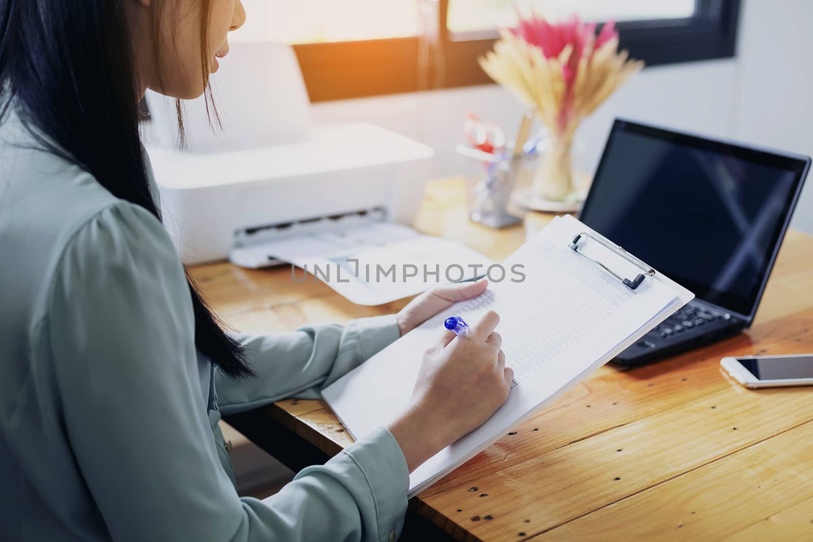 Beautiful young businesswoman doing some paperwork while sitting at office desk in front of computer.